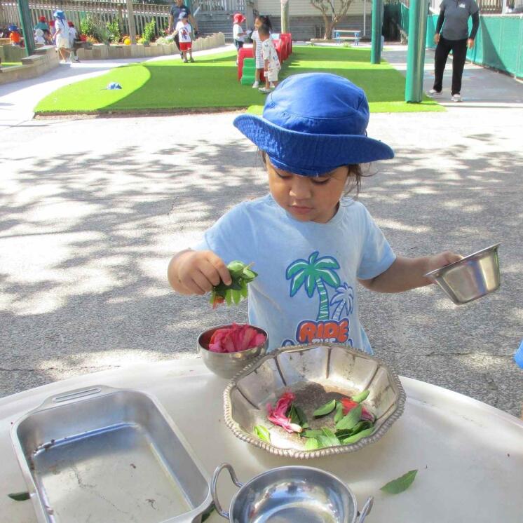 Preschool girl engaged in fun sensory play outdoors for education in Otahuhu Preschool at Busy Bees